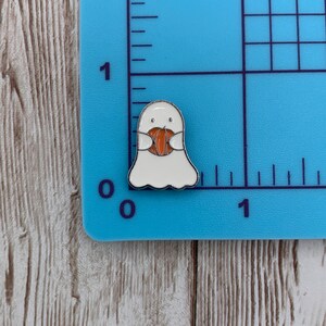 Peut inclure: Un fant&ocirc;me blanc avec un visage amical tenant une citrouille orange. Le fant&ocirc;me est bord&eacute; d'argent et a des yeux noirs. La citrouille est bord&eacute;e de noir.