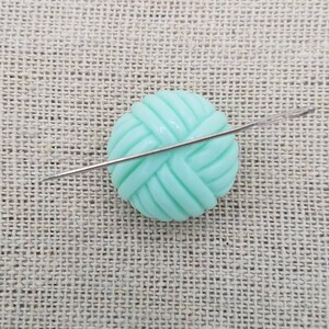 May include: A light green yarn ball with a silver knitting needle going through it.