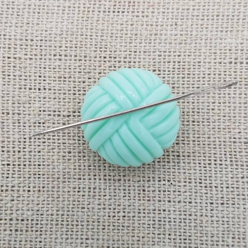May include: A light green yarn ball with a silver knitting needle going through it.