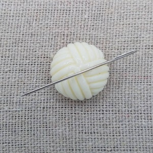 May include: A white plastic button shaped like a ball of yarn with a silver needle going through it.