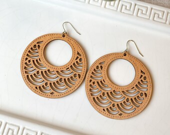 Könnte beinhalten: Ein Paar große, runde Holzohrringe mit einem filigranen, komplizierten Muster. Die Ohrringe sind hellbraun und haben ein schlichtes, elegantes Design.