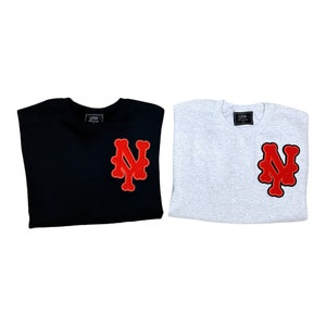 May include: Two t-shirts, one black and one heather grey, with a red felt New York City logo on the front. The logo is a stylized letter N with a Y inside.