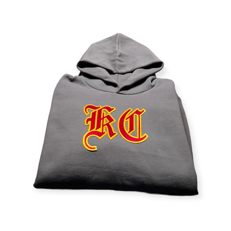May include: A gray hooded sweatshirt with a red and yellow "RC" logo in a gothic font.