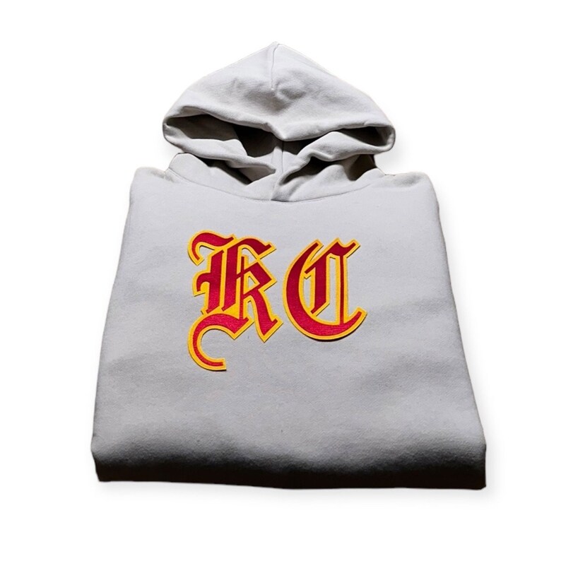 May include: A gray hooded sweatshirt with a red and yellow embroidered "RC" logo.