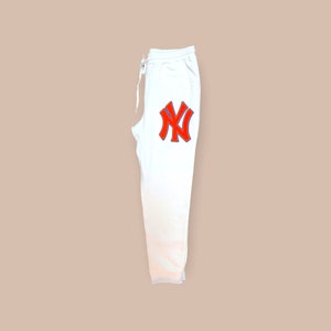May include: White sweatpants with a red and blue New York City logo on the left leg.