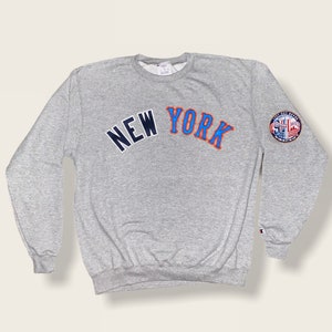 May include: Gray sweatshirt with the words "NEW YORK" in blue and orange lettering on the front. A small patch with the words "East River Warriors" is on the right sleeve.