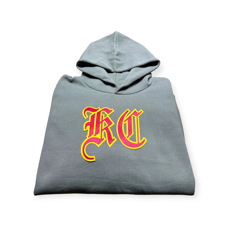 May include: A gray hooded sweatshirt with a red and yellow "RC" logo in a gothic font.