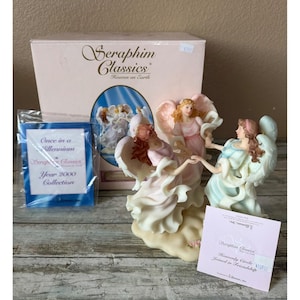 Puede incluir: Una taza de cerámica blanca con un asa negra y el texto "But First, Coffee" en negro, con una fuente de estilo manuscrito. La taza está sobre una superficie blanca.