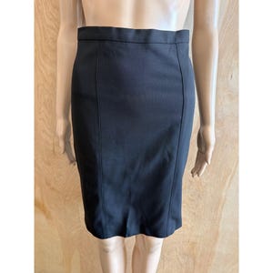 May include: A black pencil skirt with a high waist and a knee-length hem. The skirt has vertical seams down the front and back, creating a tailored silhouette. The fabric appears to be a smooth, woven material.