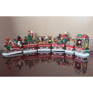May include: A decorative Christmas train set featuring multiple connected cars with pug figurines, Santa Claus, and elves. The train cars are painted in red, green, and white with text including Pug Christmas Express, Happy Pug Holidays, Pug Park, I Love Pugs, and Santa's Pug Salon.
