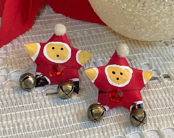 May include: A pair of red and yellow star-shaped earrings with a white pom-pom on top. Each earring has a red button, a red jewel, and two gold bells.