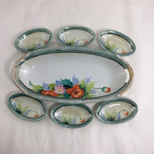 Puede incluir: Un juego de fuentes vintage. El juego incluye una fuente ovalada grande y seis fuentes ovaladas más pequeñas. Cada pieza es blanca con un borde verde azulado y un diseño floral con flores rojas, rosas y azules. La fuente tiene detalles dorados.