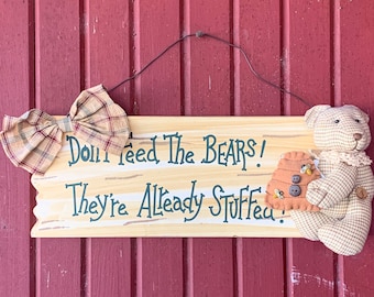 May include: A wooden sign with a plaid bow and a stuffed bear holding a honeycomb. The sign reads "Don't Feed The Bears! They're Already Stuffed!"