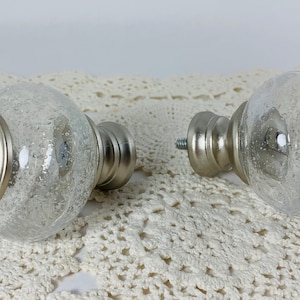 May include: Two silver and clear glass curtain finials with a textured glass design. The finials are round and have a silver metal base.