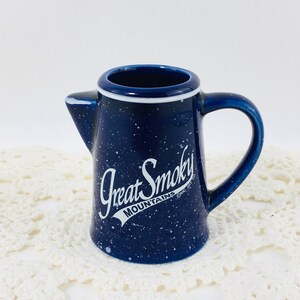 May include: A blue ceramic creamer with white speckles and a white design that says "Great Smoky Mountains" in a cursive font.