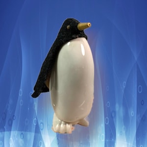 Può includere: Una statuetta di pinguino in ceramica bianca con un mantello in tessuto nero e un beccuccio dorato.