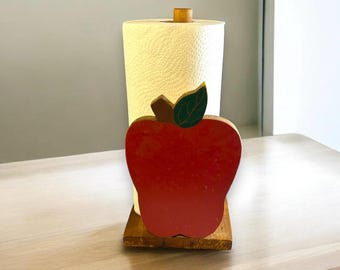 Könnte beinhalten: Papierrollenhalter aus Holz in Form eines roten Apfels mit einem grünen Blatt. Der Halter steht auf einem Holzsockel und hat eine Rolle Papierhandtücher darauf.
