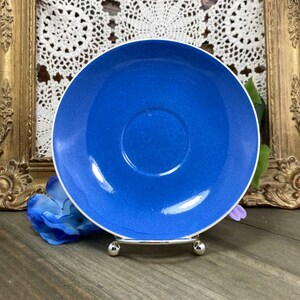 May include: A blue ceramic saucer with a white rim, sitting on a decorative stand with three legs.