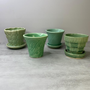May include: Four small ceramic plant pots in various shades of green. One has a scalloped rim and bubble texture, one features embossed leaf patterns, one is a smooth tapered pot, and one has a textured basket-weave design with a matching saucer.