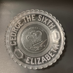 May include: A clear glass commemorative plate with a raised design of a crown, swords, and the text "GEORGE THE SIXTH CORONATION ELIZABETH 1937".