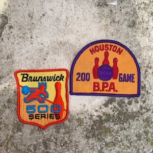Può includere: Due toppe ricamate, una gialla con il testo "Houston 200 Game B.P.A." e l'altra arancione con il testo "Brunswick 500 Series" e un cartone animato di birilli e palla.