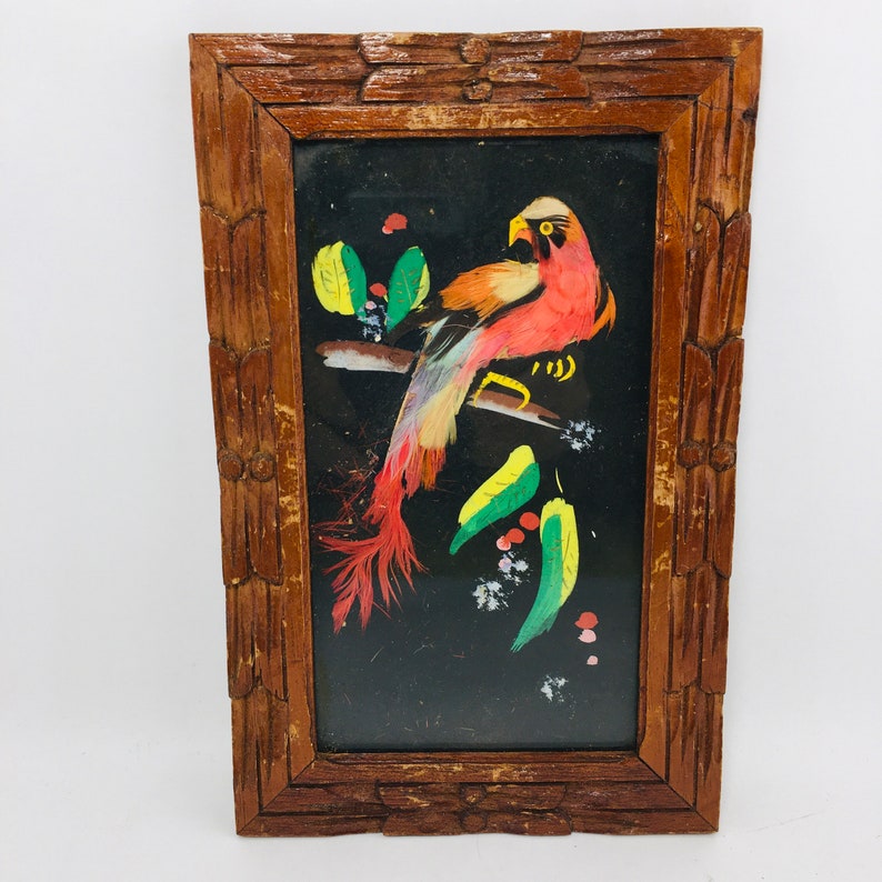 Peut inclure: Une &oelig;uvre d'art encadr&eacute;e repr&eacute;sentant un oiseau color&eacute; fait de plumes, sur un fond noir. L'oiseau est perch&eacute; sur une branche avec des feuilles vertes et des baies rouges.