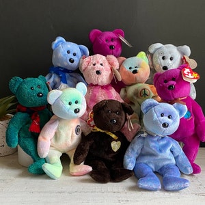 May include: A group of nine plush teddy bears in various colours, including blue, green, pink, brown, and purple. The bears are all sitting on a white surface.