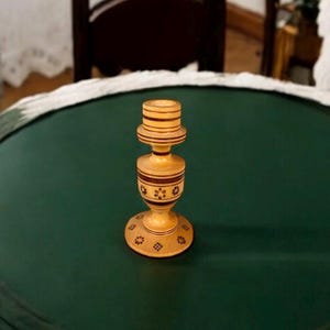 May include: A wooden candle holder with a brown and white striped design and floral patterns. The holder has a round base and a cylindrical body.
