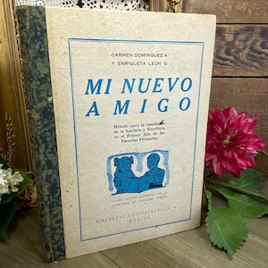 以下が含まれることがあります： 「Mi Nuevo Amigo」というタイトルのヴィンテージブック。青い縁取りと、読書をする2人の子供たちのイラストが描かれています。この本は、小学校1年生の読み書きを教えるための方法です。メキシコの教育公務員省の承認を得て、Empresas Editoriales, S.A.から出版されています。