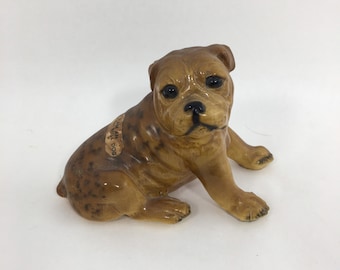May include: A brown and black figurine of a bulldog puppy sitting with its paws tucked under its body. The figurine has a label that reads "English Bull Dog".