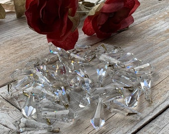 Puede incluir: Un montón grande de prismas de cristal transparente en forma de lágrima con bucles de alambre dorado. Los prismas están esparcidos sobre una superficie de madera marrón claro.