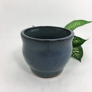 May include: A small, blue ceramic pot with a rounded bottom and a slightly flared rim. The pot has a dark blue glaze with a subtle sheen.