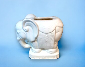 Puede incluir: Maceta de cerámica blanca en forma de elefante con detalles intrincados y una base. La maceta está diseñada para contener plantas o flores.