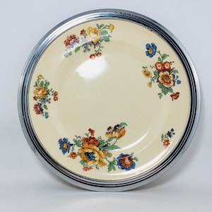 May include: A white ceramic plate with a silver rim and a floral design. The flowers are yellow, orange, red, blue, and green.