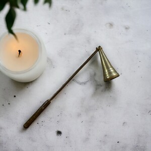 May include: A brass candle snuffer with a long handle. The snuffer is designed to extinguish a candle flame safely.