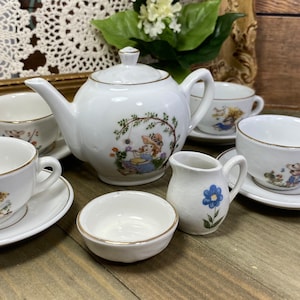 Könnte beinhalten: Ein weißes Porzellan-Tee-Set mit floralem Design. Das Set beinhaltet eine Teekanne, vier Teetassen, vier Untertassen und einen Milchkännchen. Die Teetassen und Untertassen haben einen goldenen Rand.