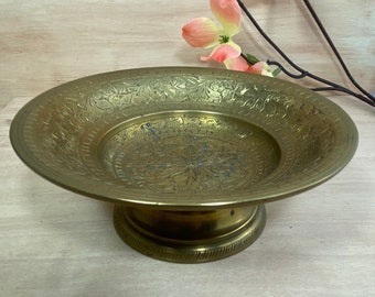 May include: A gold-colored metal bowl with intricate floral designs etched into the surface. The bowl sits on a pedestal base.