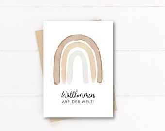 May include: A white card with a watercolor rainbow in shades of brown and beige. The text "Willkommen auf der Welt!" is printed in black below the rainbow.