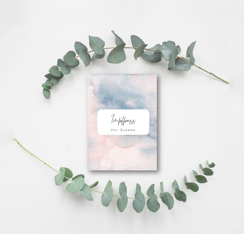 May include: A small, rectangular notebook with a watercolor design in shades of pink and blue. The cover features a white rectangular label with the German words "Impfpass" and "Vor- Zuname" in black script. Eucalyptus branches frame the notebook.