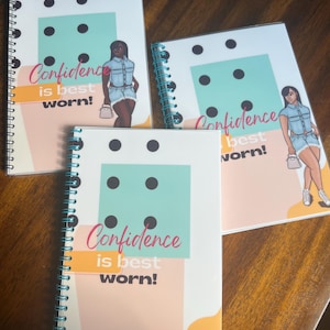 May include: Three spiral bound notebooks with a teal, orange, and yellow geometric design. Each notebook features a black and white illustration of a woman wearing a denim outfit and the text "Confidence is best worn!"