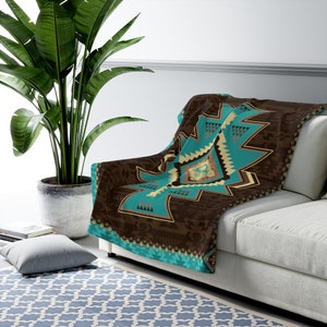 May include: A brown and turquoise patterned throw blanket with geometric designs. The blanket is folded and draped over a white couch.