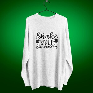 heather gray sweatshirt with shake your shamrocks text design on a hanger against a green background
