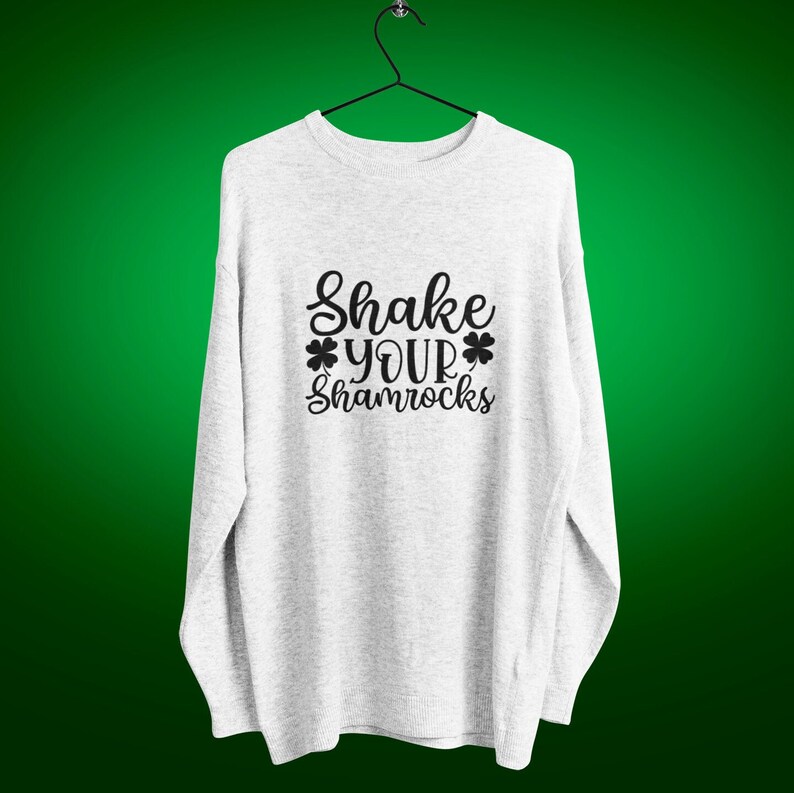 heather gray sweatshirt with shake your shamrocks text design on a hanger against a green background