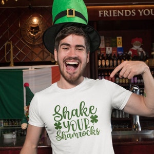 man in a bar pointing at his shirt with shake your shamrocks text design wearing a green leprechaun hat