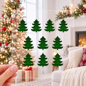 May include: A clear rectangular sheet featuring ten dark green glittery Christmas tree shapes arranged in three rows. The trees are uniform in design, displaying a classic pine silhouette with layered branches and a pointed top.