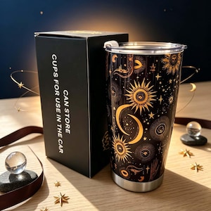 May include: A black tumbler with a gold celestial pattern featuring suns, moons, and stars, paired with a black box labeled CAN STORE CUPS FOR USE IN THE CAR. The tumbler has a clear lid and a silver base, showcasing a detailed cosmic design.