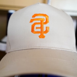 May include: A white baseball cap with an orange embroidered "SF" logo.