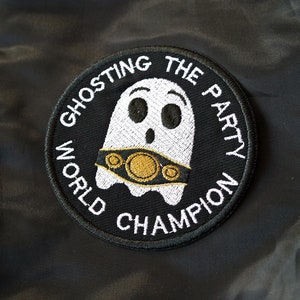 Può includere: Toppa ricamata nera con un fantasma bianco che indossa una cintura da campione dorata. Il testo intorno al fantasma recita "Ghosting the Party World Champion".
