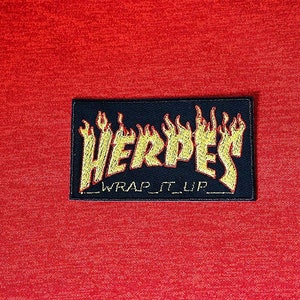 May include: Red hoodie with a drawstring. A black patch with yellow flames and the word "HERPES" is sewn on the front. Below the word "HERPES" is the text "_WRAP IT UP_".
