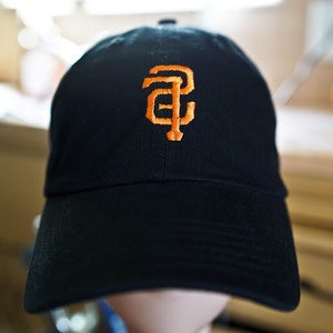 Peut inclure: Une casquette de baseball noire avec un logo "SF" brodé en orange.